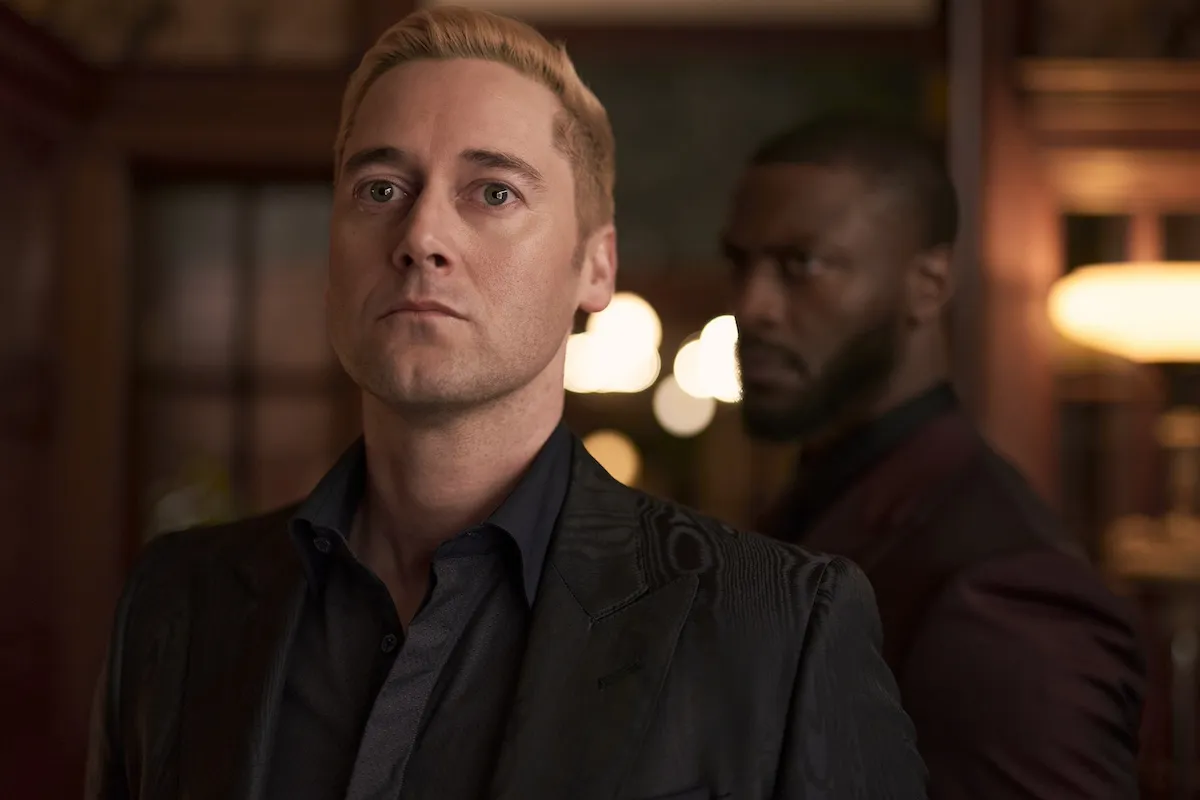 Stone-faced man with bleached blond hair looking forward with Alex Cross lurking in the background